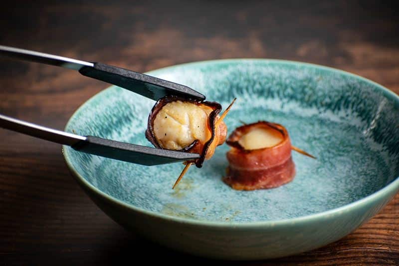 Cooked bacon-wrapped scallops on a blue plate.