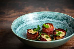 Cooked bacon-wrapped scallops on a blue plate with garlic butter and parsley.