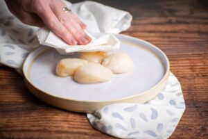 Fresh scallops being dabbed with a paper towel, wood background.