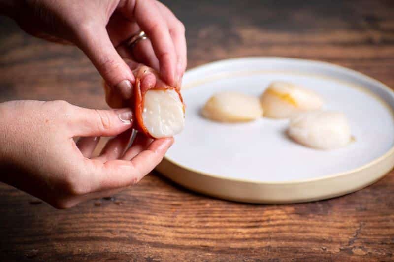 Woman's hands wrapping bacon around a scallop.