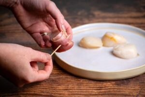 Woman's hands inserting a toothpick into bacon.