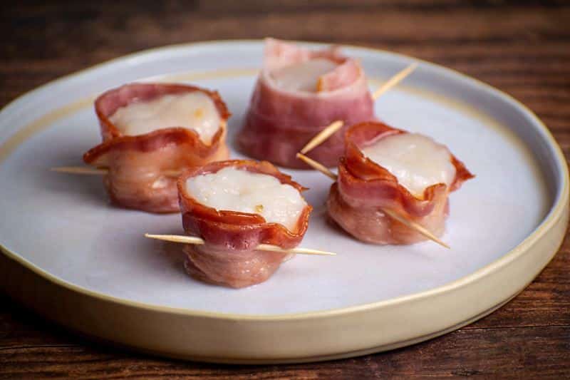4 scallops on a plate wrapped in bacon and closed with a toothpick.