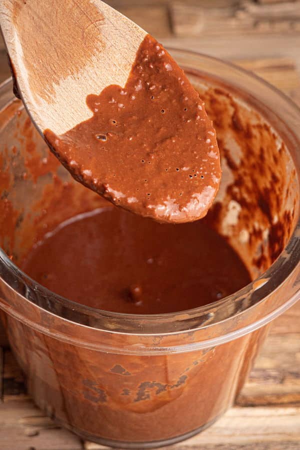 Mole sauce blended in a processor, wooden spoon with mole sauce on it, wooden background.