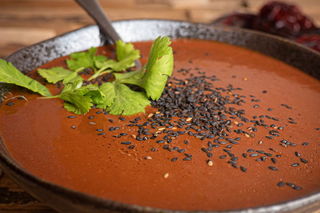 Mole sauce in a bowl with cilantro and black sesame seed toppings, wooden background, dried peppers in the background.