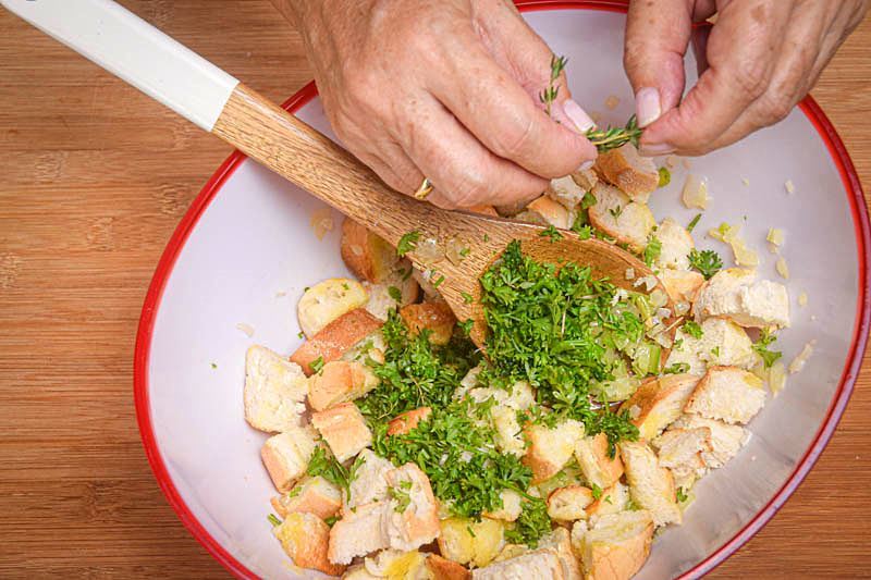 Stuffing in a bowl, thyme being added to mix, wooden spoon.