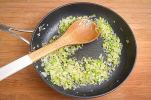 Onions fried in a pan, with wooden spoon, wooden background.