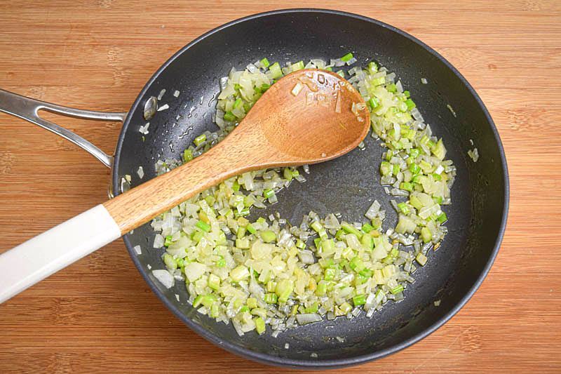 Onions fried in a pan, with wooden spoon, wooden background.