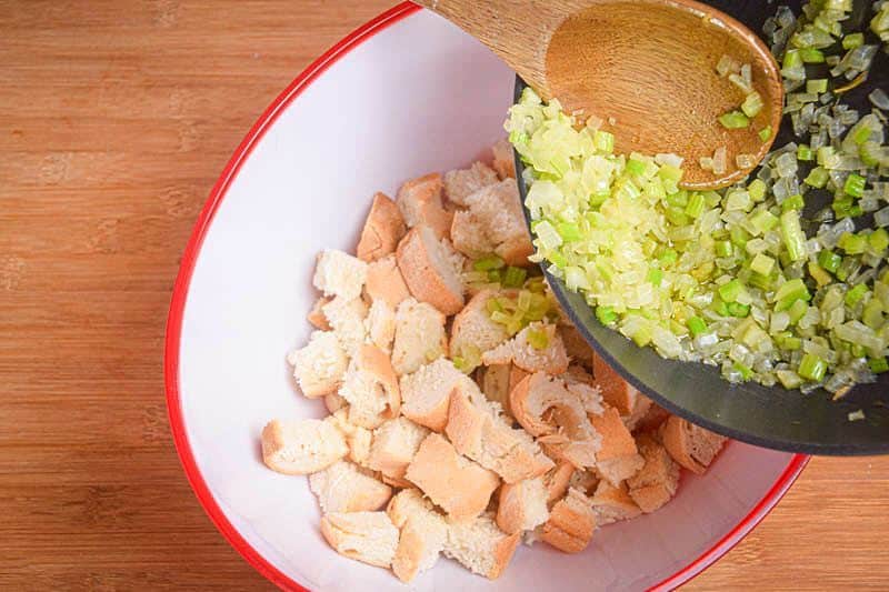 Fried onion being added to stuffing bread with a wooden spoon.