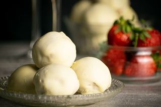 Strawberry Champagne Cake Balls on a clear dish, black background. Glasses of champagne in the background and strawberries.