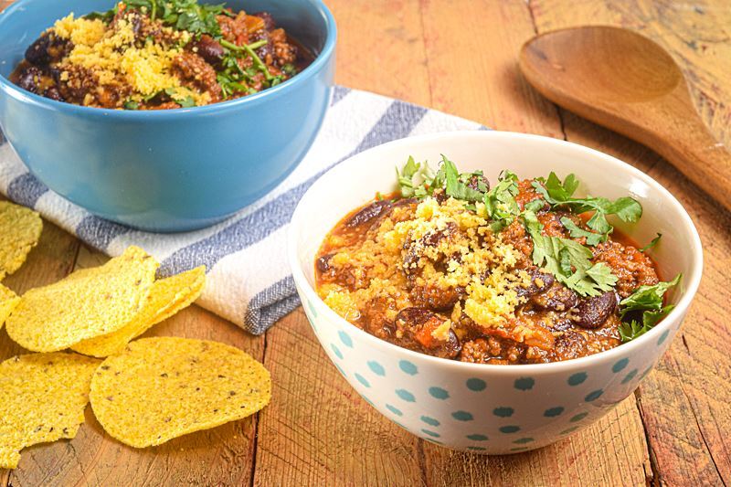 Electric Skillet Chili in a white bowl with blue polka dots, wooden background, tortillas chips on the side.