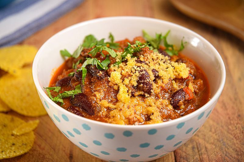 Electric Skillet Chili in a white bowl with blue polka dots, wooden background, tortillas chips on the side.