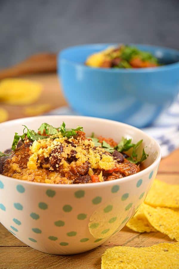 Electric Skillet Chili in a white bowl with blue polka dots, wooden background, tortillas chips on the side.