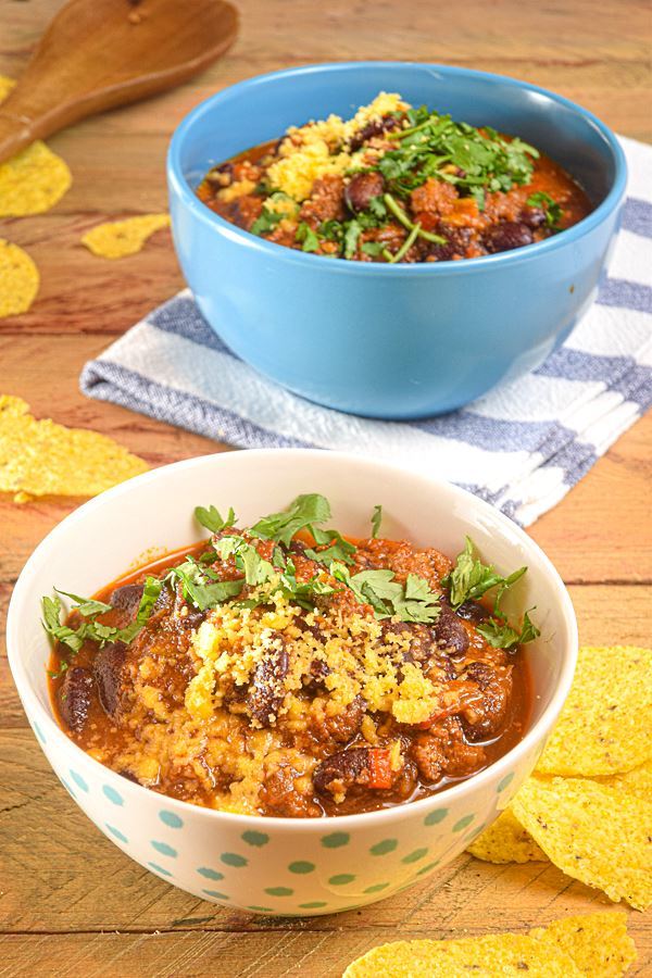 Electric Skillet Chili in a white bowl with blue polka dots, wooden background, tortillas chips on the side. and a wooden spoon.