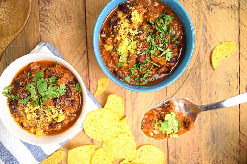 Electric Skillet Chili in a white bowl with blue polka dots, wooden background, tortillas chips on the side. and a spoon of chili