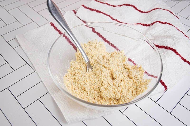 Mixed apple crisp ingredients in a clear glass bowl, white background.