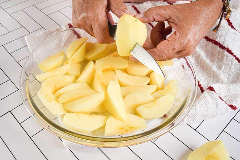 Apples getting sliced into a clear glass bowl.