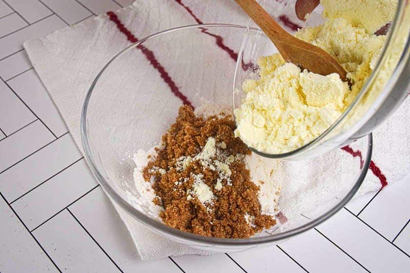 Powdered milk being added to bowl of apple crisp ingredients.