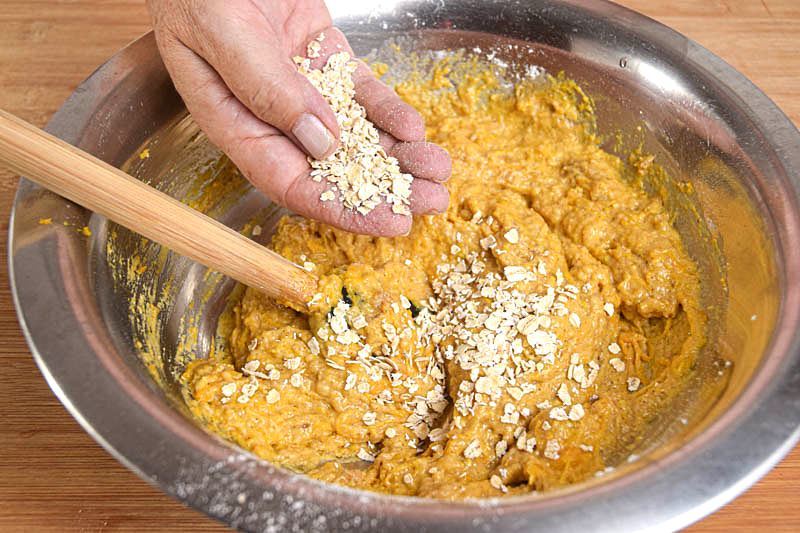 Pumpkin Muffins with cranberries batter in a metal bowl, a hand sprinkling in the oats.