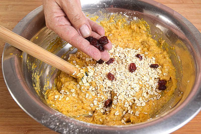 Pumpkin Muffins with cranberries batter in a metal bowl, a hand sprinkling in the cranberries.