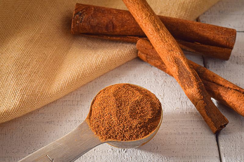 Ground cinnamon in a measuring spoon, whole cinnamon sticks on the side.
