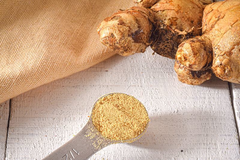 Ground ginger in a measuring spoon, fresh whole ginger on the side.