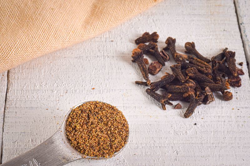 Ground cloves in a measuring spoon, whole cloves on the side.