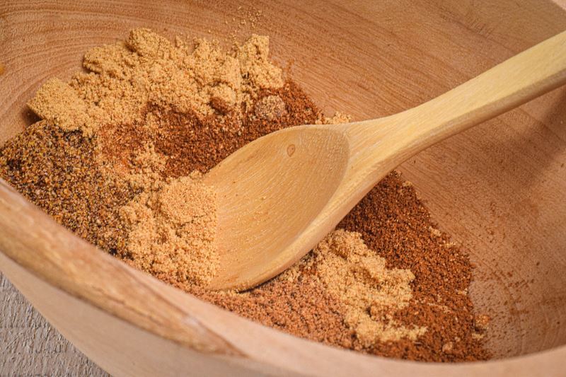 A wooden bowl full of pumpkin pie spice mix and a small wooden spoon.