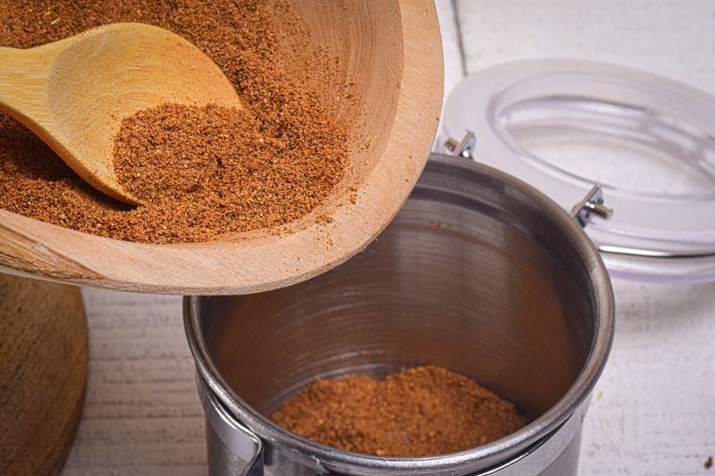 Pumpkin pie spice getting transferred from wooden bowl to metal canister.