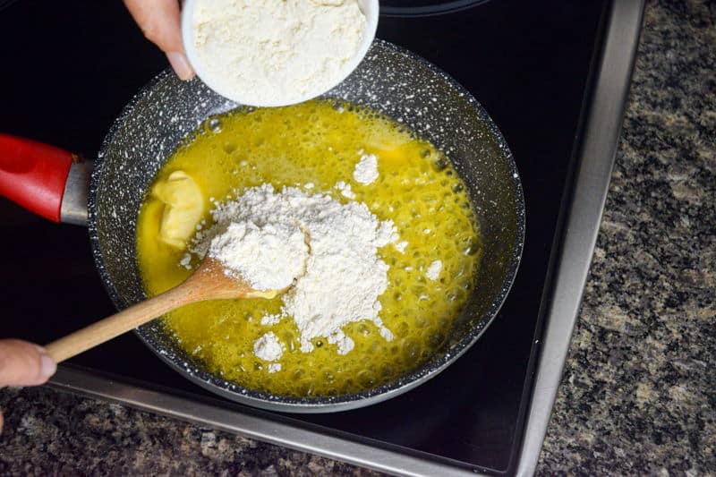 A ramekin of flour being added to melted butter in a frying pan.