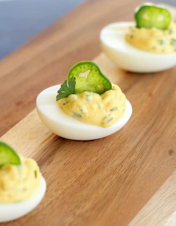 Deviled eggs with slices of jalapeno on top, wooden background.