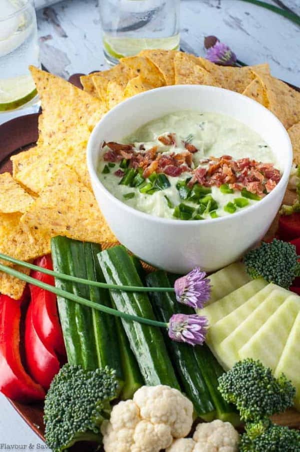 Bacon and chive jalapeno dips in a small white bowl, tortillas and vegetables for dipping on the side.
