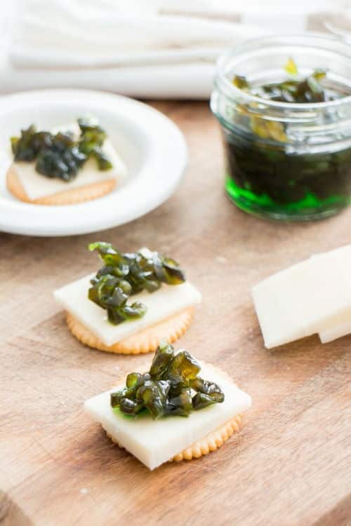 Candied jalapenos on cheese and crackers, wooden background.