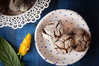 Chocolate crinkle cookies on a white plate, with yellow flowers on the side, blue background.