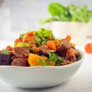 Electric Skillet Beef Stew in a white bowl, cherry tomatoes on the side, white background.