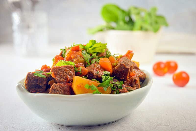 Electric Skillet Beef Stew in a white bowl, cherry tomatoes on the side, white background.