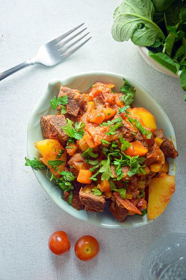 Electric Skillet Beef Stew in a white bowl, cherry tomatoes and a fork on the side, white background.