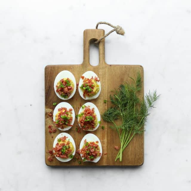 Deviled eggs and dill on a wooden cutting board.