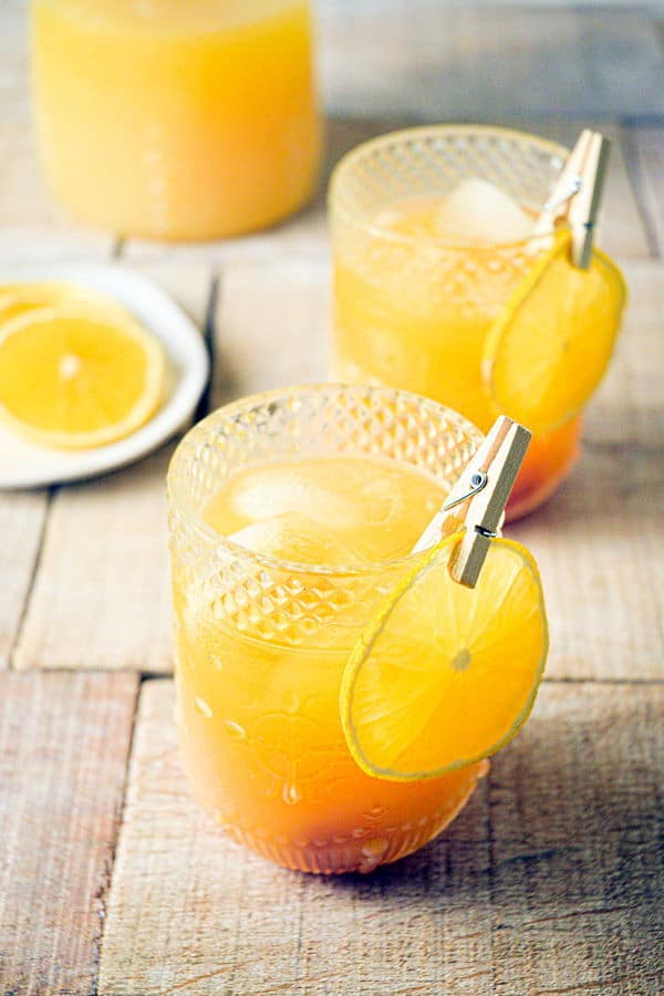 Fall Pumpkin Party Punch in a clear glass with a thin orange slice garnish clipped on with a clothespin, orange slices on a plate in the background.