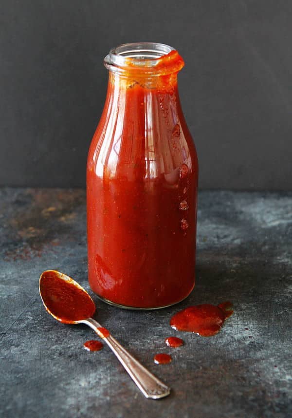 Homemade BBQ sauce in a bottle, spoon with sauce on the side, dark background.