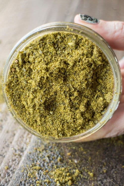 Chili powder in a clear glass bowl, a hand holding it over wooden background.