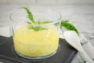 Dill sauce in a clear glass bowl, dill and spoon on the side.