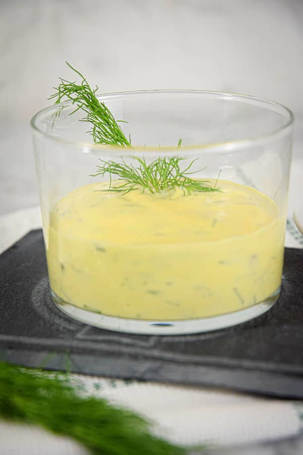 Dill sauce in a clear glass bowl, fresh dill on the side.