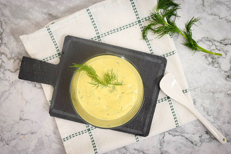 Dill sauce in a clear glass bowl, dill and spoon on the side.