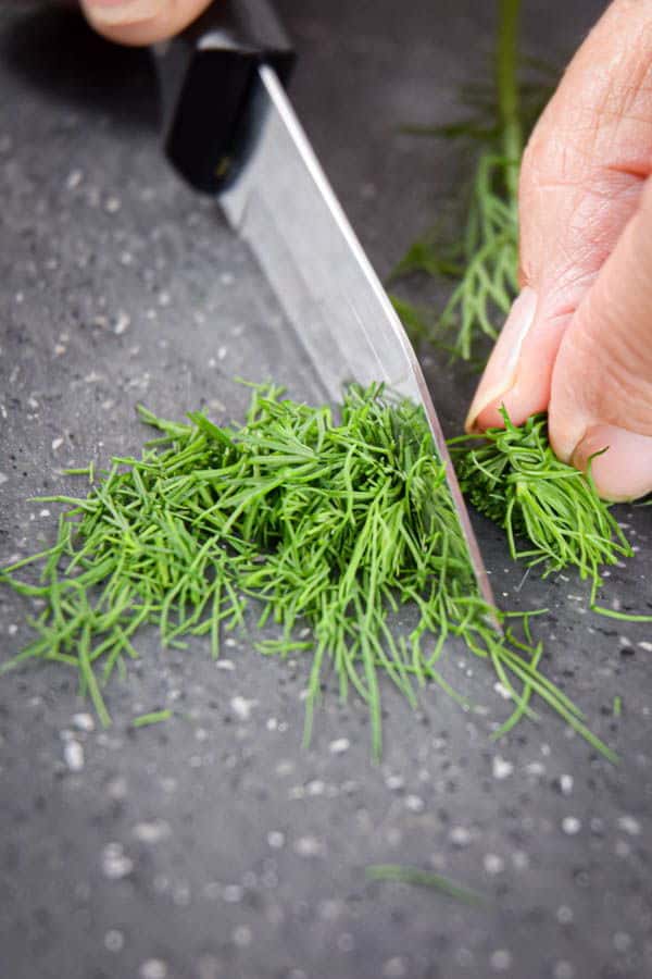 Chopping dill up close on grey cutting board.