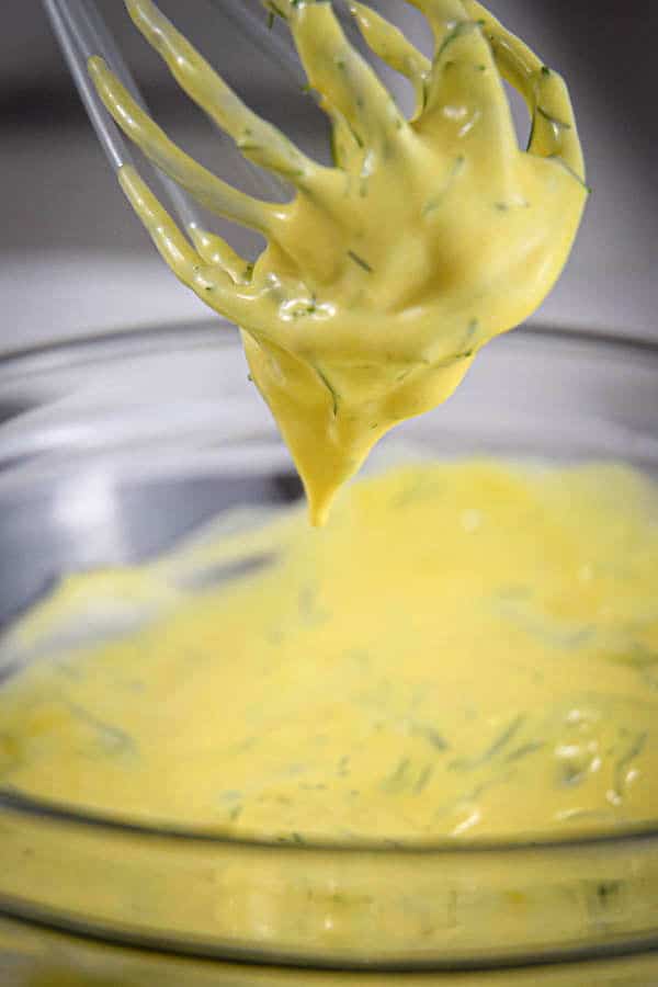Dill sauce mixed up with a whisk in a clear glass bowl.