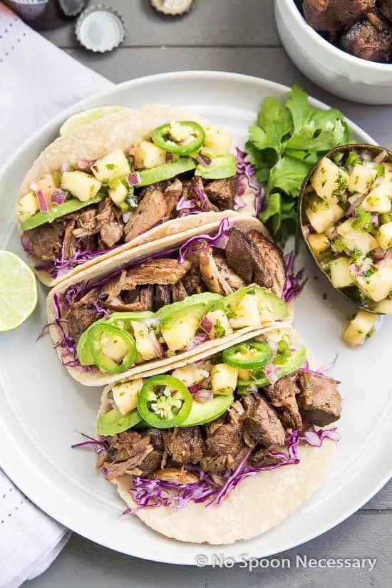 Jerk pork carnita tacos on a white plate, wooden background.