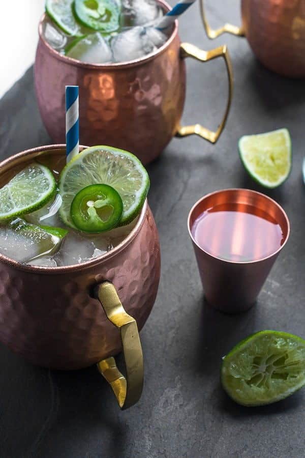 Moscow mule in copper mugs with limes slices and jalapeno slices scattered around.