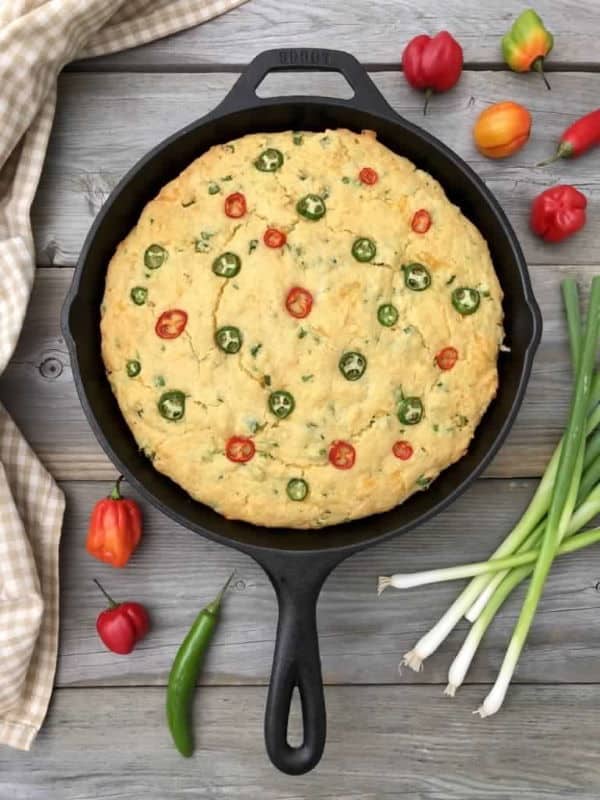 Cornbread in a cast iron skillet, green onion on the side on wooden background.