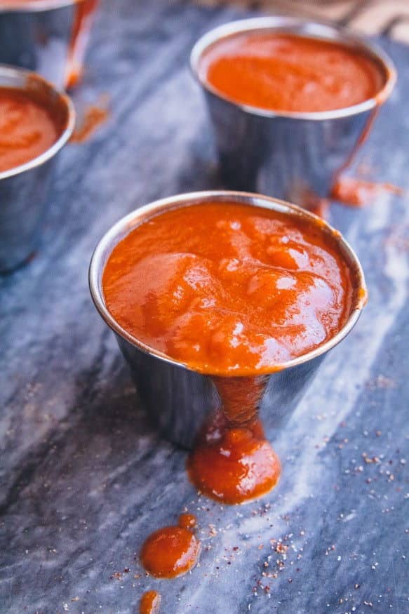 Sweet and spicy barbecue sauce in small metal cups, dark marble background.