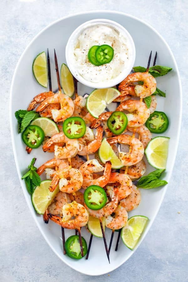 Tequila jalapeno shrimp skewers with a small bowl of dip on white serving dish.